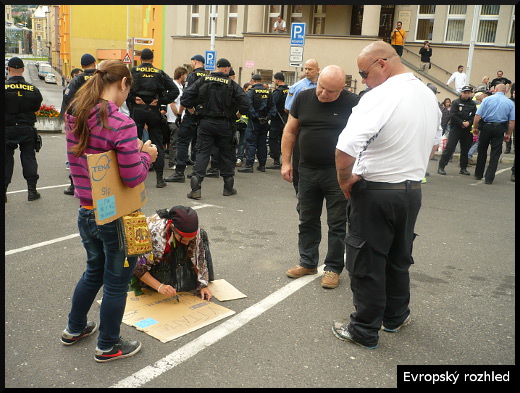 Ivanka Mariposa Čonková po poslechnutí projevu Tomáše Vandase připravuje nový transparent s nápisem Vítáme migranty. Pozoruje jí Petr Žák.